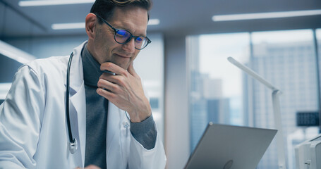 Aufkleber - Male Doctor in a High-tech Hospital Office Works on a Laptop, Analyzing Medical Data. the Modern Clinical Environment Highlights Advanced Healthcare, Research