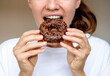 © Barillo_Images - Front view closeup photo of young woman eating chocolate donut.