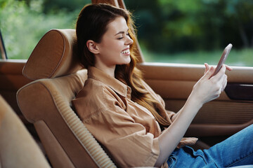 Canvas Print - Young woman smiling while using smartphone in a car, wearing a casual brown shirt, green background, representing happiness and leisure.