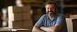 © felix_brönnimann - Warehouse setting with smiling man in casual attire, representing logistics, supply chain management, and small business success with packaging boxes.