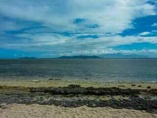 Wall Mural - Tranquil seascape at Green Island, Great Barrier Reef. Rocky shoreline with volcanic formations against crystal-clear turquoise waters. Vibrant blue sky with white clouds. Queensland tropical paradise