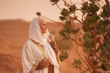 Wall Mural - Elegant Senior Woman in Traditional White and Gold Shawl Standing in Open Field at Sunset