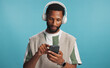 © peopleimages.com - Headphones, phone and black man in studio with music, playlist or album for review on blog. Type, audio tech and African male influencer listening to song online for streaming app by blue background
