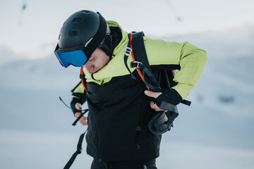 Wall Mural - A man wearing skiing equipment is adjusting his gear on a snowy mountain slope under clear winter skies, preparing for winter sports activities.