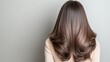 © Viktoriia Kan - A person with long, shiny hair is facing away, showcasing natural waves and layers. The smooth texture shines under soft indoor lighting against a plain wall