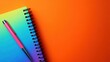 © Artittaya - A bright and colorful shot of a notebook and pen against a bold orange backdrop