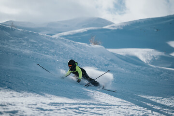 Wall Mural - A skier in winter sportswear loses balance while skiing on a snowy slope in a mountainous area with bright daylight and snow-covered scenery. Captured action conveys adventure, activity, and fun.