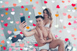 © deagreez - Beautiful couple of muscular handsome man and charming blonde woman in white underwear, guy making selfie on smart phone, girl standing on knees, embracing him from back, woman's day morning