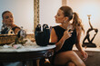 © qunica.com - A woman applies perfume while sitting in a chic room, her reflection visible in the ornate mirror, exuding elegance and sophistication.