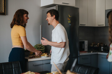 Wall Mural - A young couple shares laughter and joy while preparing food in a modern kitchen setting, creating a warm and cheerful atmosphere.