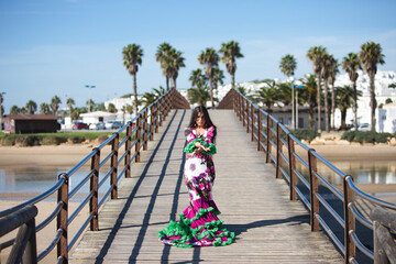 Wall Mural - Latin woman, brunette, with flowing hair, dancing flamenco on a wooden catwalk by the seashore. The woman is wearing a white dress with a floral print and ruffles. Intangible Cultural Heritage.