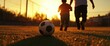 © Design By Reiga - Father and son playing soccer at sunset, field background. Family leisure activity