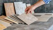 © Iona - A hand picking a large, beige tile from a spread of varied tones and finishes, representing creativity in design choices.