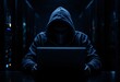 © Dmitry - Mysterious hooded hacker in dark room working on laptop. Cybercrime and network security threat concept. Dark silhouette at night with blue glow from screen. Data center background
