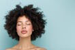 © Photopia - Young woman with curly afro hairstyle, glowing skin and natural makeup, serene beauty portrait, eyes closed, isolated on light blue background, minimalist and radiant look, trendy concept.
