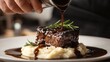 © azi - Chef pouring rich sauce over tender beef short rib served with creamy mashed potatoes and rosemary.