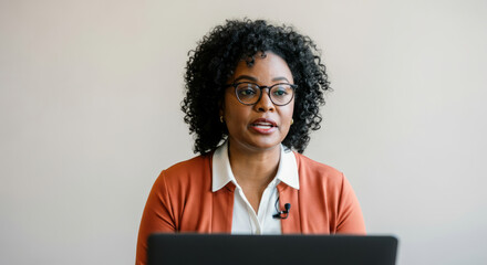 Canvas Print - A woman wearing glasses and an orange jacket is sitting in front of a laptop