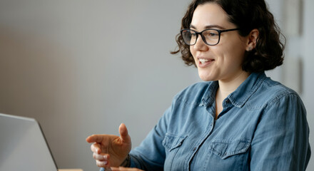 Canvas Print - A woman wearing glasses is sitting at a desk with a laptop in front of her