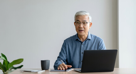 Canvas Print - An older man sits at a desk with a laptop and a notebook