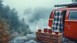 © otter2 - A retro red camper van parked on a misty mountain cliff, a cozy plaid blanket draped over an open back door, steaming coffee mugs on a wooden crate beside it