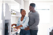 © peopleimages.com - Happy, cooking and black couple in kitchen with love for dinner, lunch or diet meal together. Smile, care and African man hugging woman for preparing healthy supper on weekend for bonding in home.