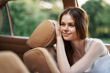 Wall Mural - Young woman smiling softly in cozy car interior, showcasing relaxed emotions and natural beauty in a lush green background, ideal for lifestyle and travel themes.