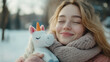 © Keitma - A cheerful young woman holding a unicorn plush toy while standing in a snowy outdoor setting. She wears a warm scarf and smiles blissfully, capturing a heartwarming and joyful winter moment.