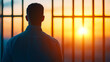© Keitma - Back view of an individual in a contemplative mood, observing a radiant sunset through a barred structure, evoking themes of introspection, hope, and reflection with empty open space in the imagery.