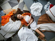 © SHOTPRIME STUDIO - A young woman in casual clothing lying on the floor surrounded by messy clothes, expressing frustration and stress in a home setting