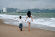 © alexkoral - back of happy mom and son walking along the beach by the sea on summer vacation