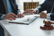 © Phimwilai - Two lawyers are discussing a contract on a clipboard, with one lawyer pointing at a specific clause with a pen, while a gavel rests on the table, symbolizing legal proceedings and negotiations