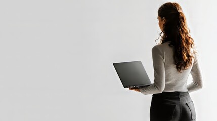 Wall Mural - Woman with brown hair holding a laptop, facing away against a neutral background.