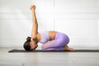 © 220 Selfmade studio - Asian woman practicing yoga in childâ€™s pose variation with arms extended upward, wearing lavender workout outfit on yoga mat in bright, minimalistic room