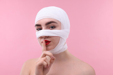 Wall Mural - Woman with nose wrapped in medical bandage after plastic surgery operation making silent gesture on pink background