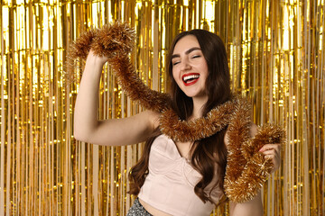 Happy young woman with tinsel against golden foil curtain