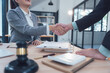 © Kritdanai - Successful Legal Partnership: Two legal professionals shake hands across a desk, signifying a successful negotiation, agreement, or partnership.  A judge's gavel rests prominently in the foreground.