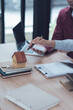© Kritdanai - Home Buying Consultation: A real estate agent and client discuss details of a potential home purchase, their hands hovering over a miniature house model.