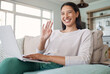 © peopleimages.com - Laptop, woman and portrait with video call for wave, greeting contact and communication on sofa. Home, female person and digital with hand gesture for virtual conversation, hello and chat application