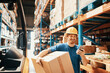 © Davor - Smiling male worker using smartphone and carrying box in large warehouse
