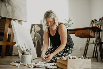 Paint, canvas and girl on floor at studio for artwork with project for passion with colour at house. Workshop, female artist and mixing with tube for oil painting with inspiration for hobby to relax.