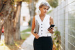 © Petro - Elderly business woman using mobile phone and walking in the autumn street