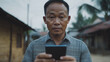 © CreativeIMGIdeas - Digital Connection: A close-up portrait of a thoughtful Asian man holding his smartphone, capturing a moment of quiet contemplation and connection in a rural setting.