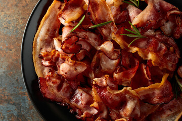 Wall Mural - Fried bacon with rosemary on a black plate.