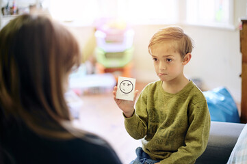 Therapy, emotion and boy talking to a therapist while sitting on a sofa in a psychology clinic. Discussion, flash card and child psychologist helping a kid with his feelings, adhd and mental health.