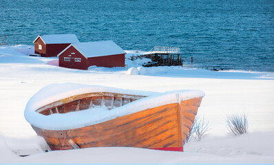 Wall Mural - brown wooden boat covered with layers of snow - beautiful winter landscape with snow covered red hou