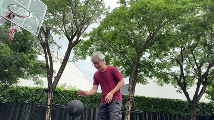 Wall Mural - A senior East Asian man is practicing and playing basketball alone in a public park.