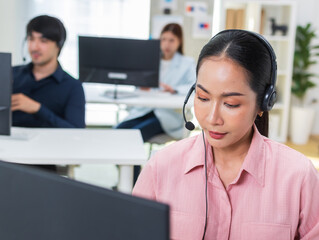 Wall Mural - Confident Asian woman working on computer for online customer support, telemarketing assistance, giving advice online using headset at call center office. Asian businesswoman customer service at work.