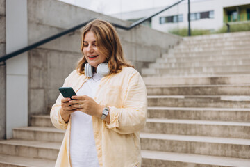 Wall Mural - Happy young woman with mobile standing on steps in city. Holidays, technology and tourism concept. Female tourist searching direction on smart phone while traveling abroad in summer