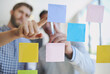 © peopleimages.com - Business people, hands or meeting with schedule planning for brainstorming, tasks or reminder at office. Closeup, employees or sticky notes with team for agenda, ideas or collaboration on glass board