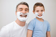 © peopleimages.com - Shaving, father and child with portrait in studio for grooming, skincare lesson and teaching hygiene. Learning, mature man and boy kid with foam cream for cleaning face or support on white background